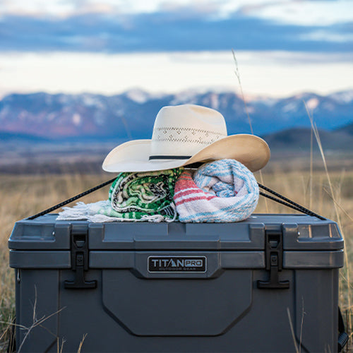 Titan PRO 55Q Roto Hard Cooler with Gear Grabber bungee cords holding picnic blankets on top of cooler