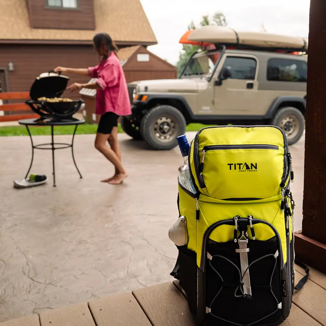 Person barbequing outside next to a backpack cooler