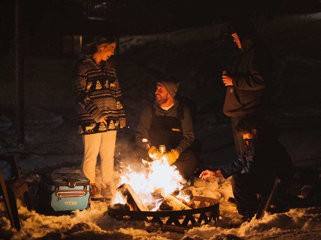 Group of friends enjoying drinks out of a Titan Cooler while having a camp fire