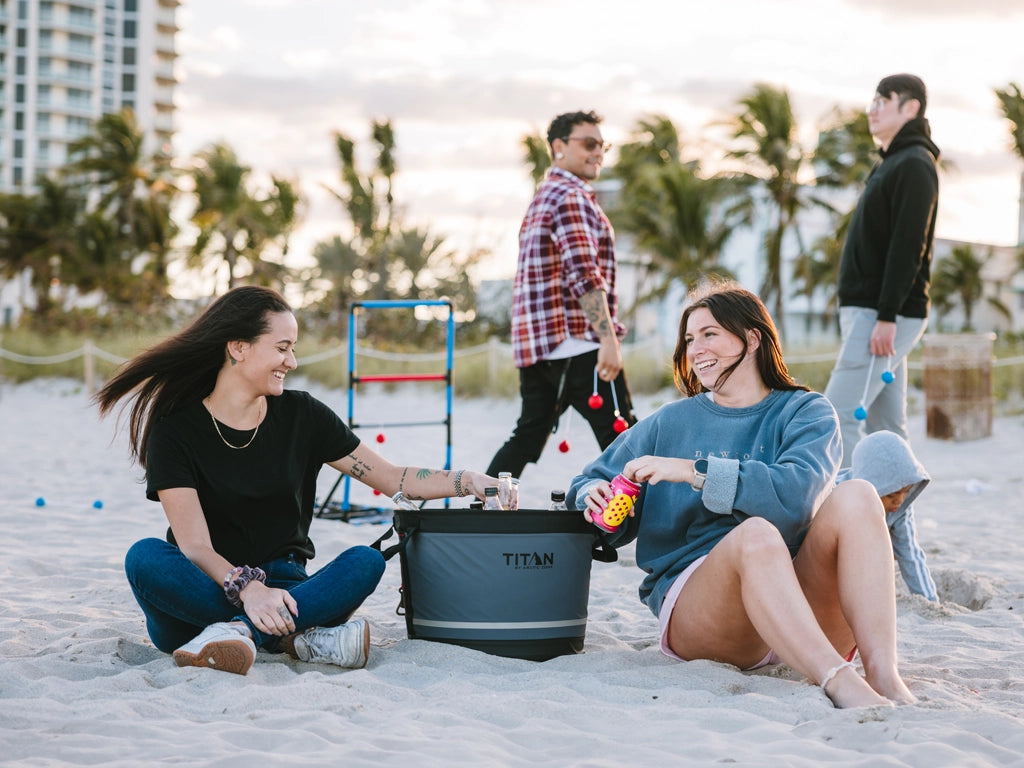 Two girls enjoying cold drinks next to Titan cooler on the beach while celebrating the 4th of July