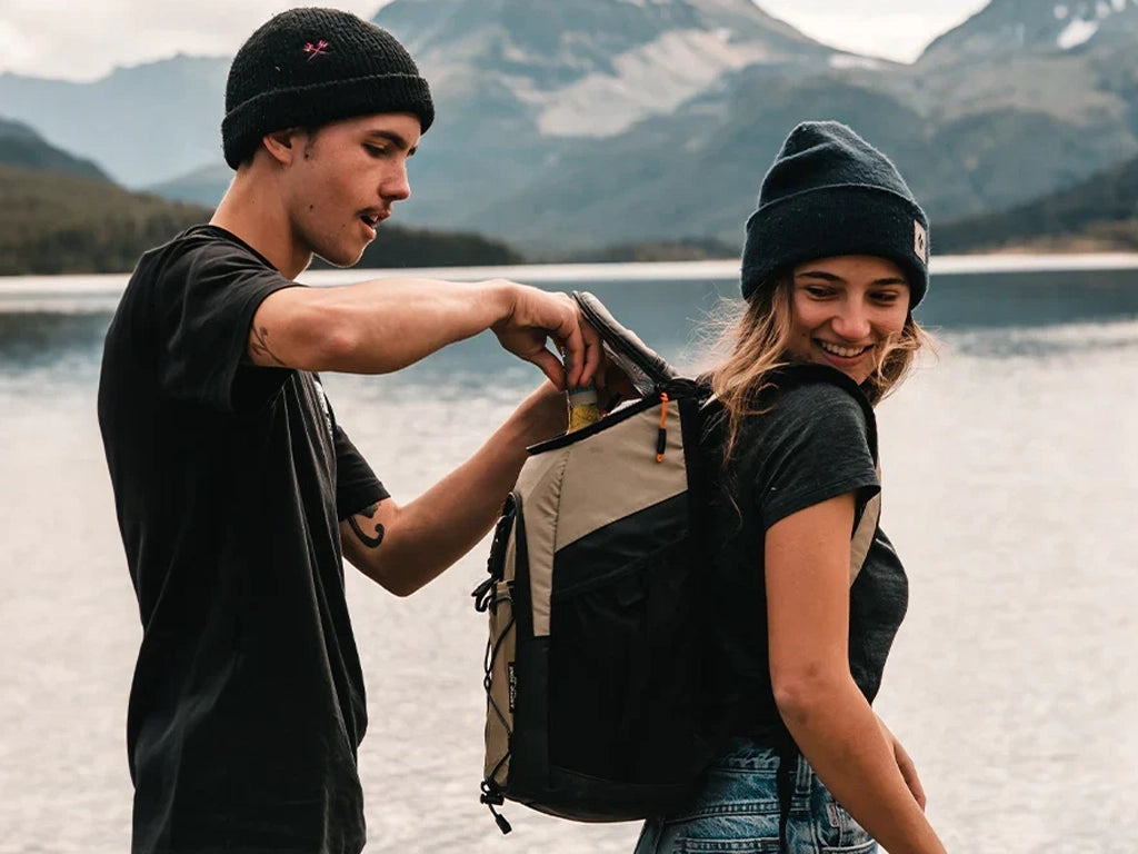 Girl wearing a Titan backpack cooler while guy reaches in to grab a cold drink