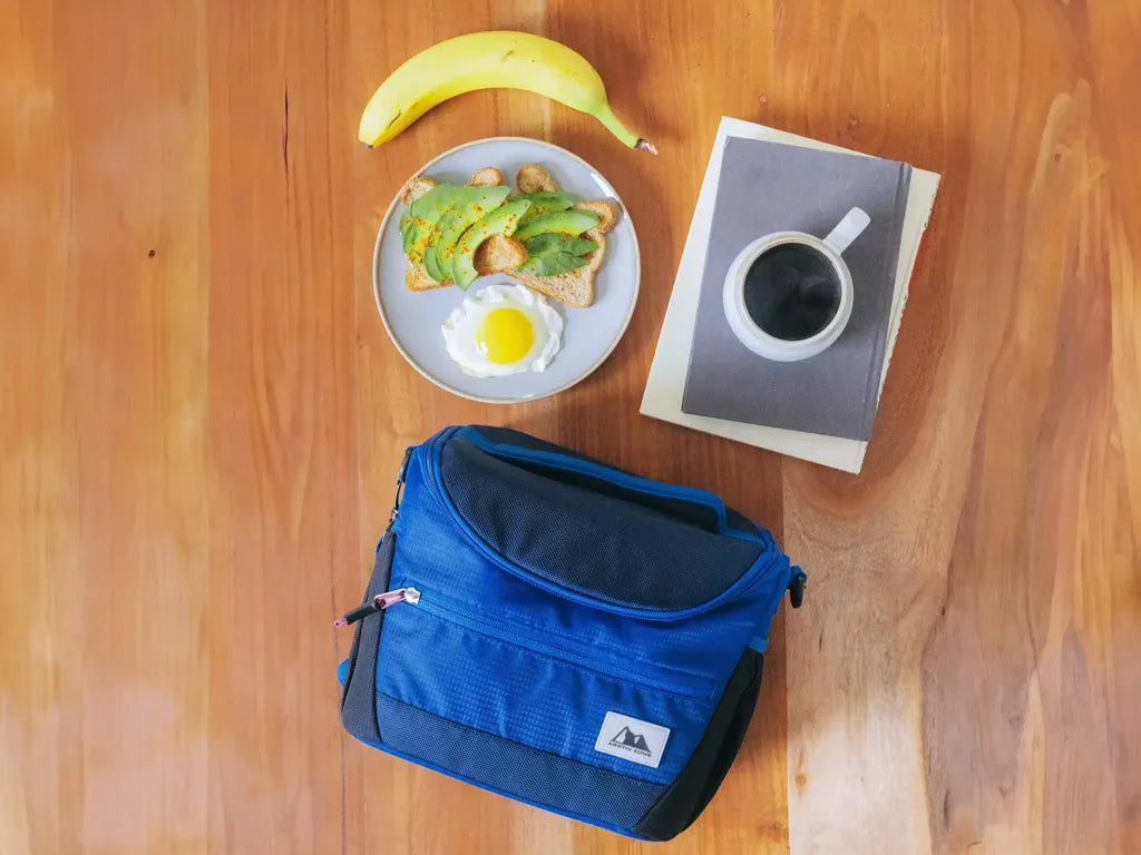 Arctic Zone Meal Prep Lunch Bag on a kitchen table beside a cup of coffee, banana and plate with food