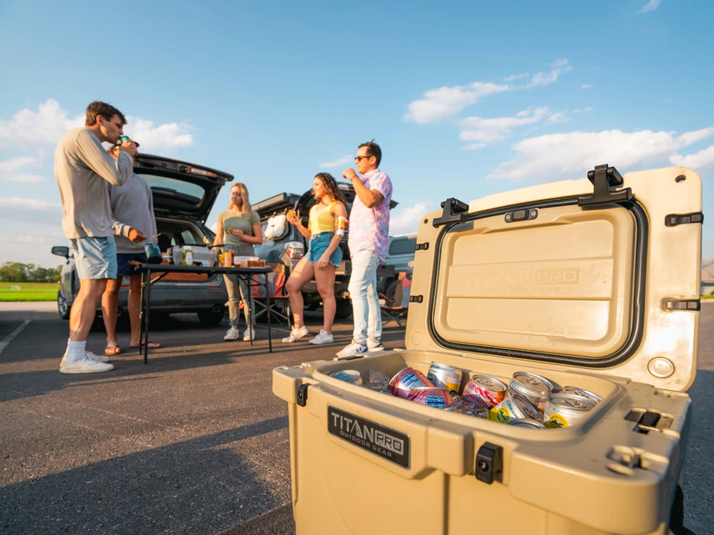 Group of friends enjoying food and drinks next to a Titan PRO Roto Hard Cooler while at a tailgate party