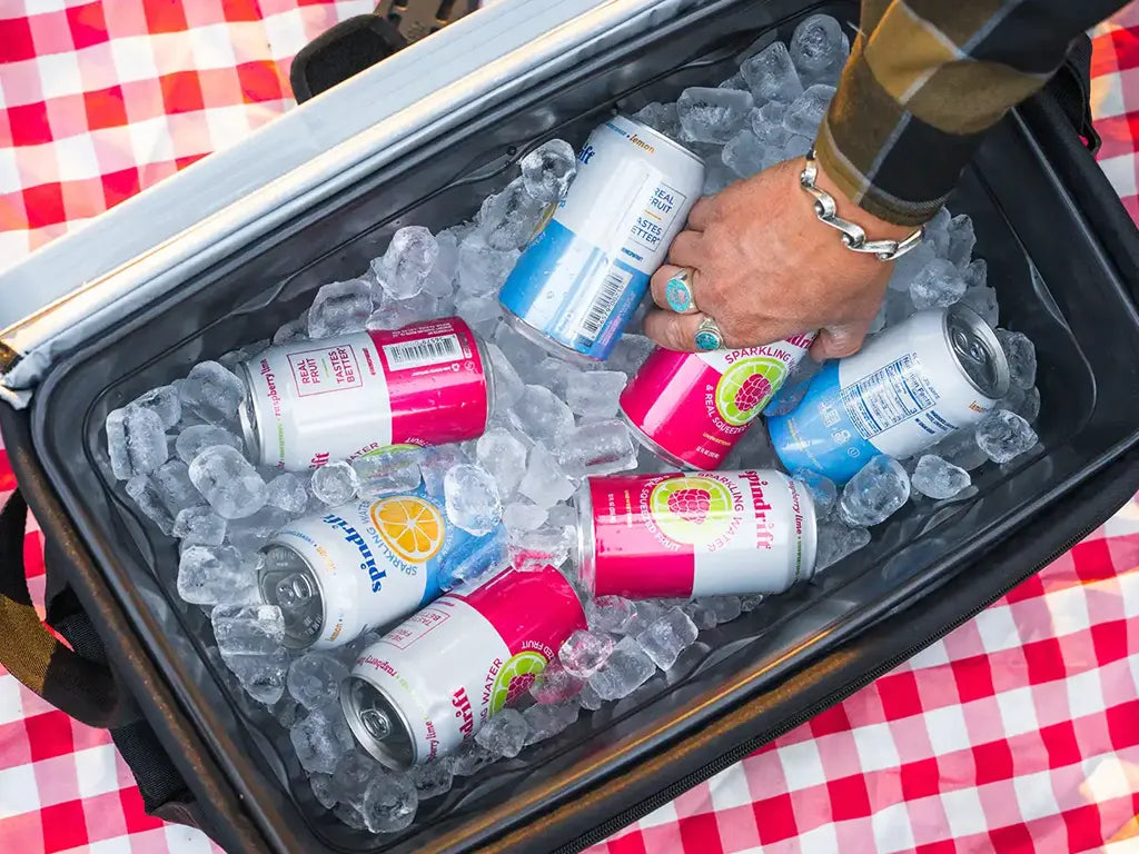 A hand reaching into a cooler full of ice cubes and cold drinks