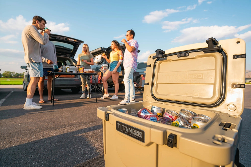 Group of friends enjoying food and drinks next to a Titan PRO Roto Hard Cooler while at a tailgate party