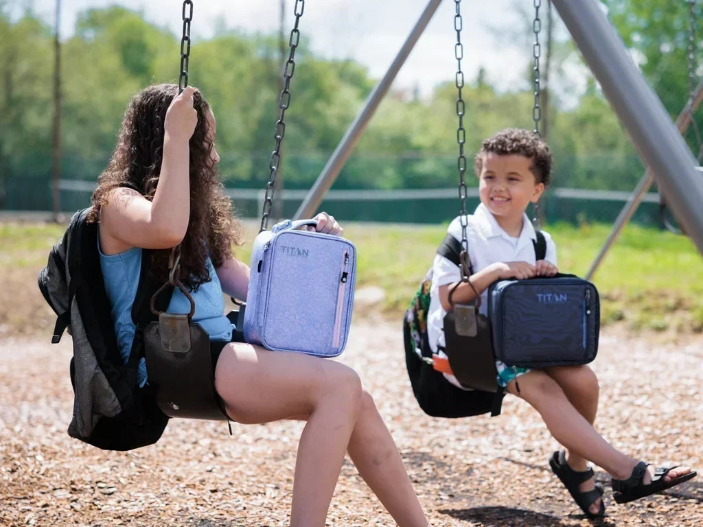 Children on playground swings with Titan by Arctic Zone insulated lunch bags for school and outdoor adventures.