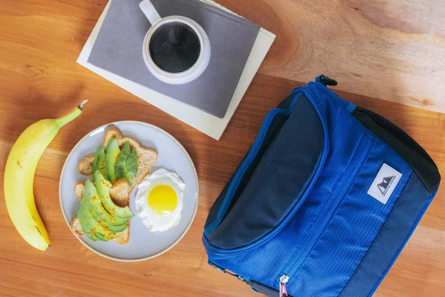 Arctic Zone Meal Prep Lunch Bag on a kitchen table beside a cup of coffee, banana and plate with food