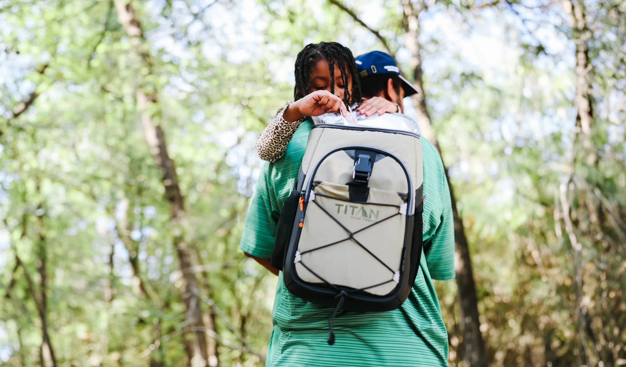 A man carrying his daughter while wearing a backpack cooler, ready for an outdoor adventure together.
