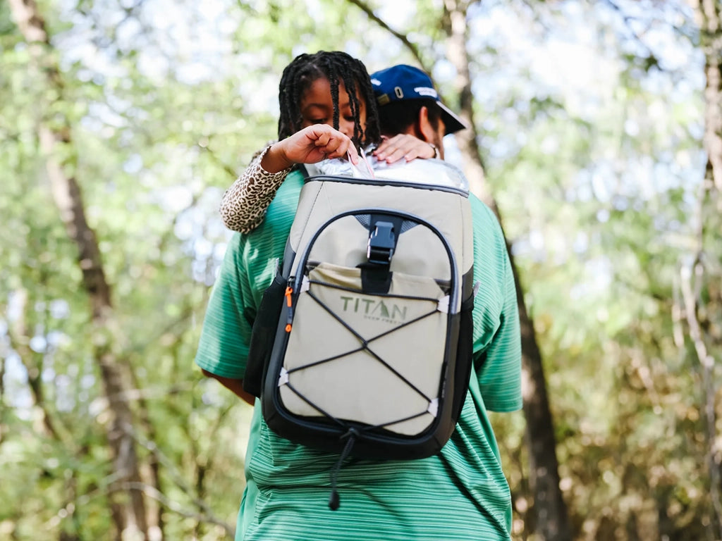 A man carrying his daughter while wearing a backpack cooler, ready for an outdoor adventure together.