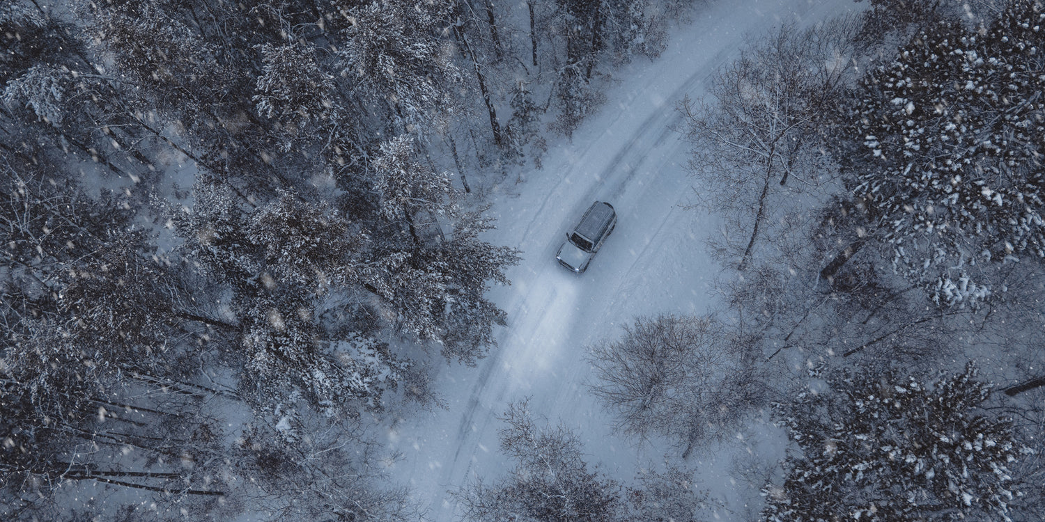 Birdseye view of a vehicle driving through a forest in the winter