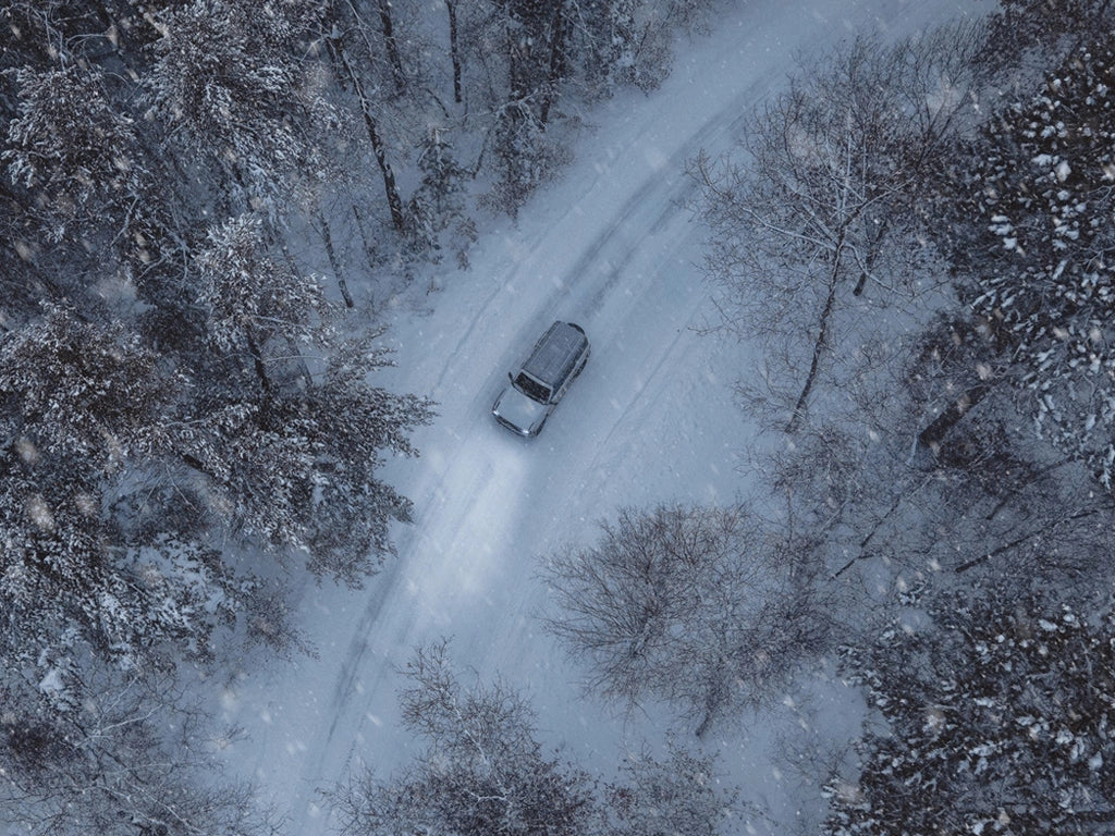 Birdseye view of a vehicle driving through a forest in the winter