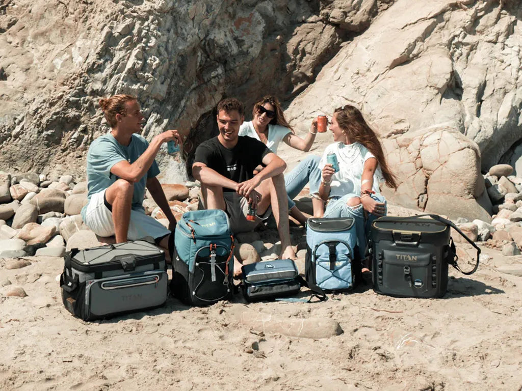 Four friends sitting together at the beach with an variety of Arctic Zone coolers