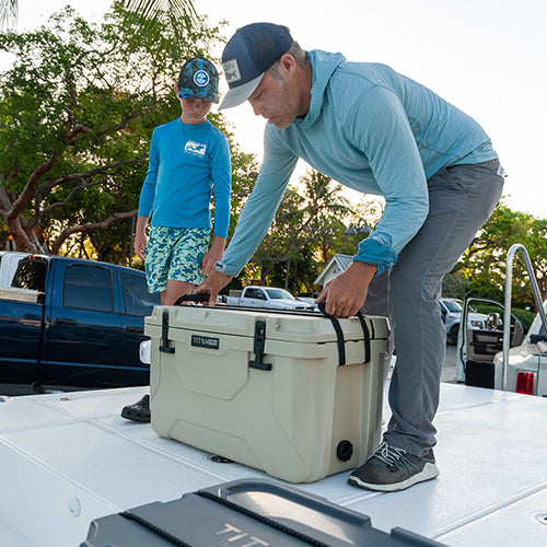 A father lifting a hard cooler off of a boat while next to his son