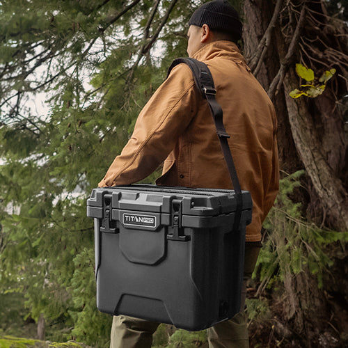 A man carrying a Titan PRO 25Q Roto Hard Cooler while in a forest