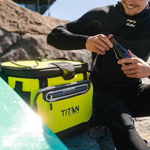 A man enjoying a cold drink next to his Zipperless cooler at the beach after a day of surfing