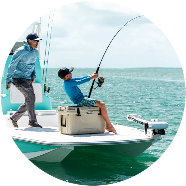 Boy sitting on a Titan PRO hard cooler while fishing with his dad