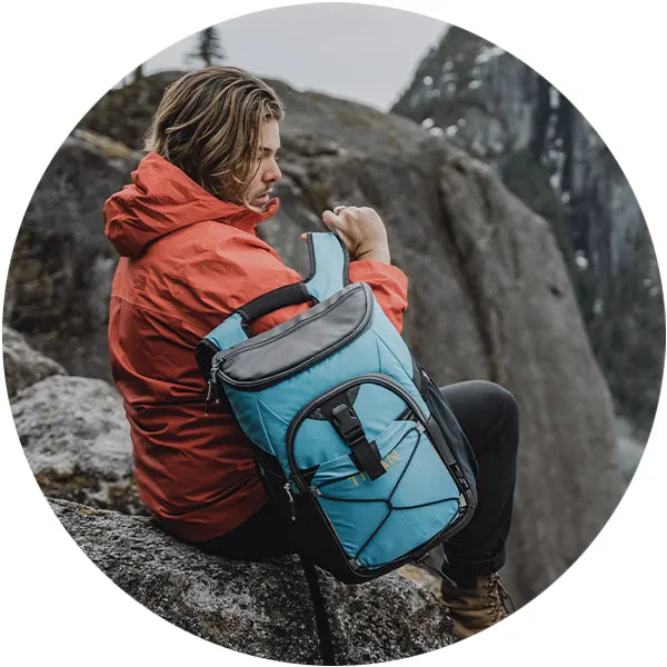 Man sitting on a rock while wearing a Titan 24 Can Backpack Cooler