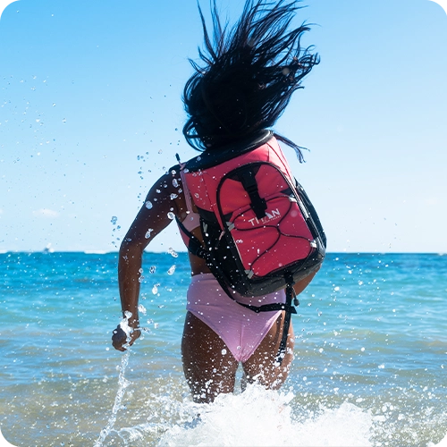 Girl at the beach, running into the ocean while wearing a Titan Backpack Cooler