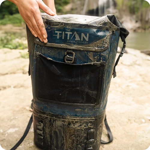 Person wiping mud from their Titan Welded Backpack Cooler