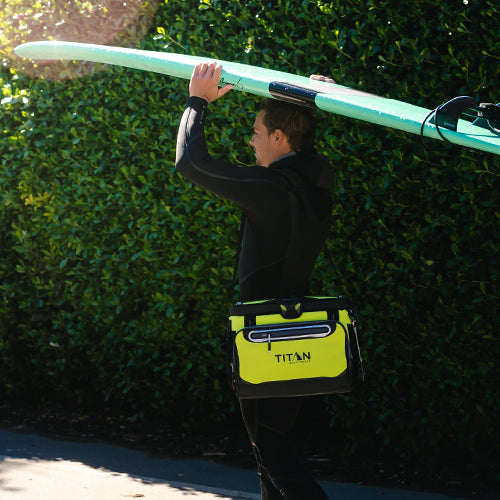 Guy carrying a surf board and Titan Zipperless Cooler while heading to the beach